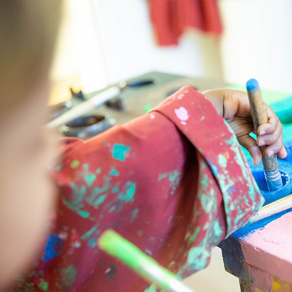 Kind steckt Pinsel in Farbe
